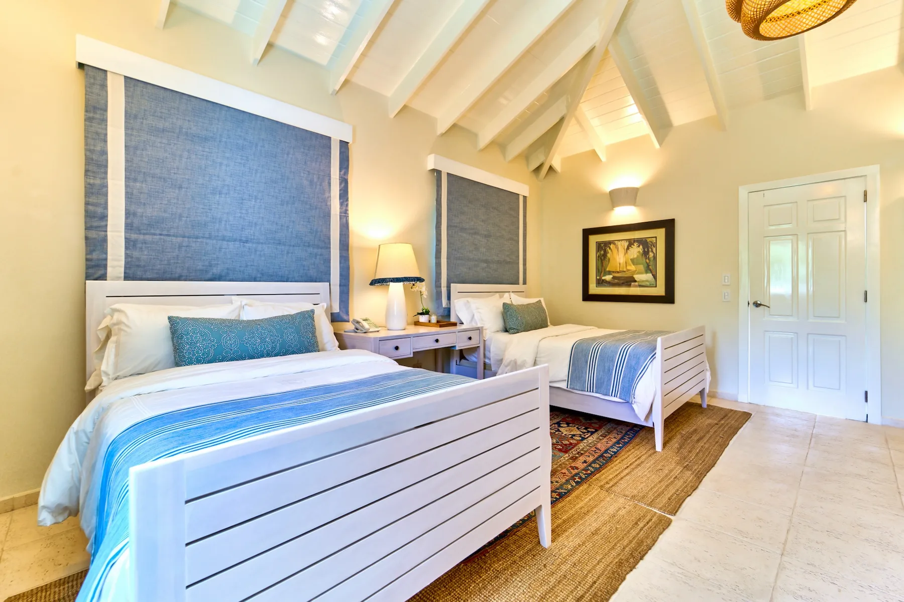 Un dormitorio luminoso con dos camas, ropa de cama azul y un techo alto abovedado.