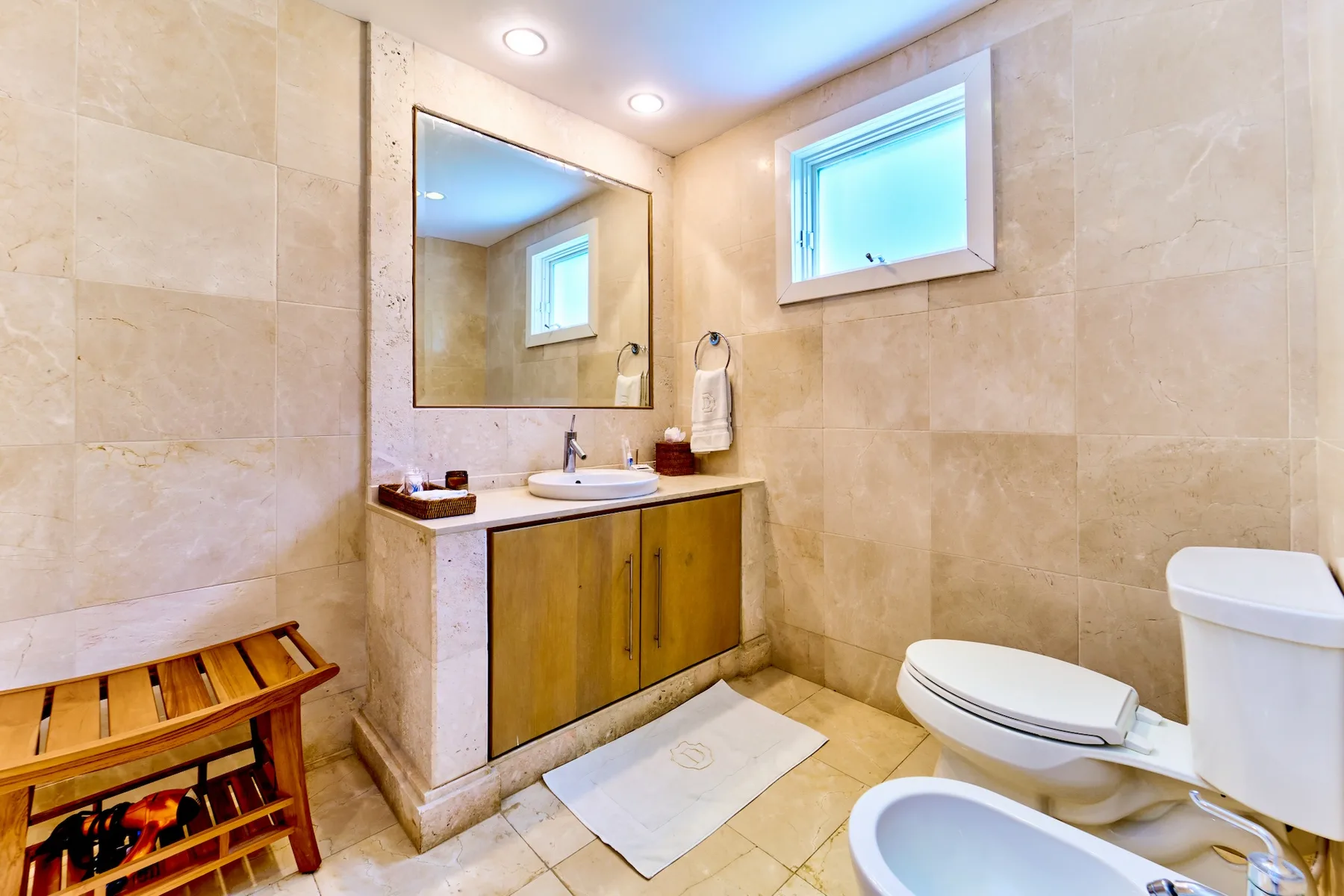 Un baño revestido de azulejos con lavabo, inodoro y una ventana pequeña.