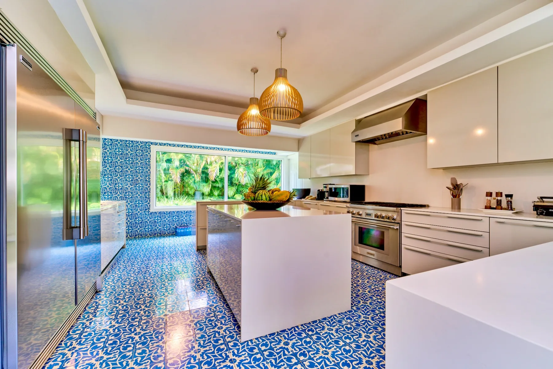 Una cocina moderna y luminosa con gabinetes blancos, una isla y suelo azul estampado.