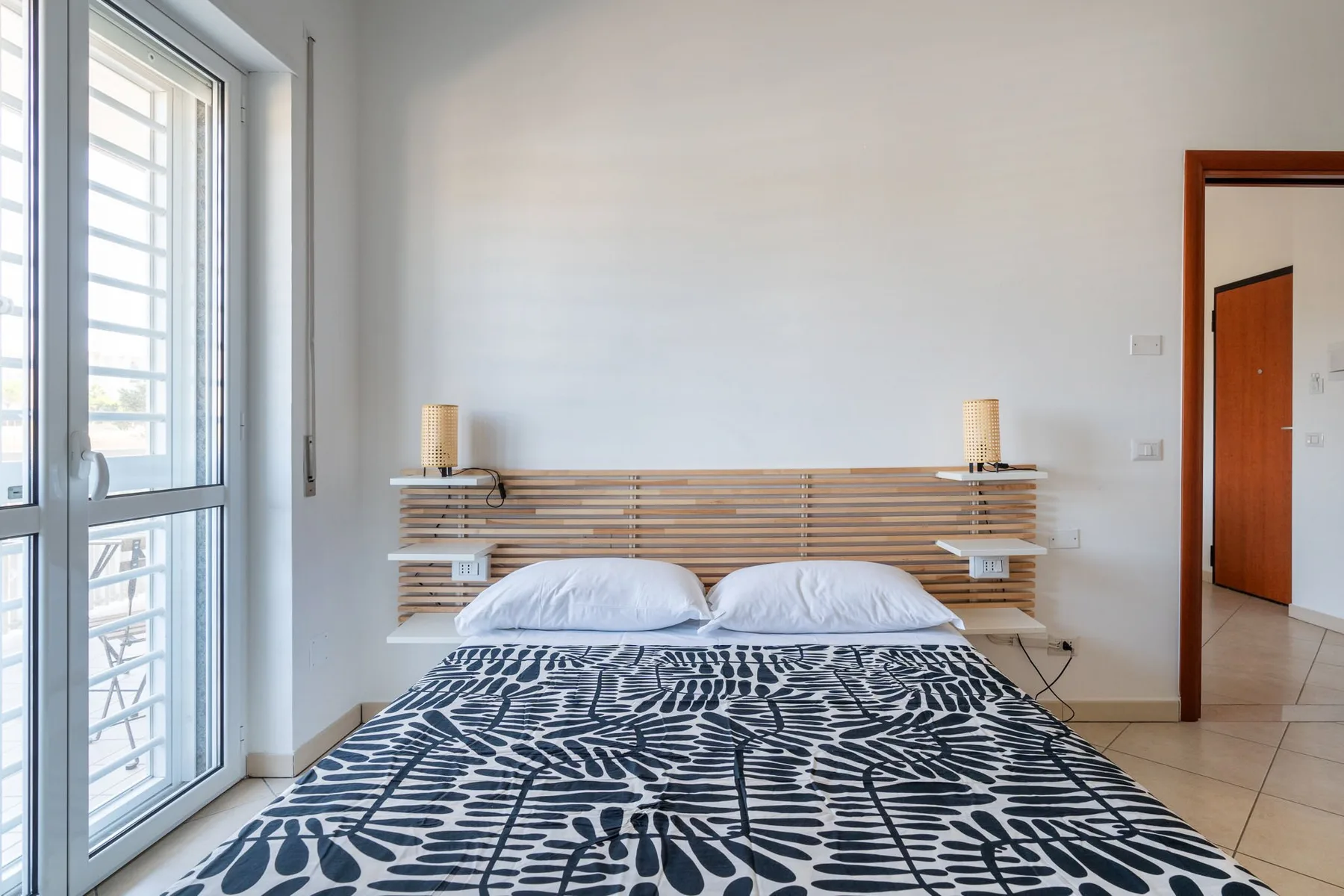 Un dormitorio con una cama cubierta con ropa de cama estampada junto a una ventana grande.