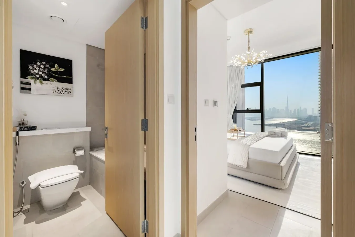Un baño da a un dormitorio luminoso con una cama junto a grandes ventanas.