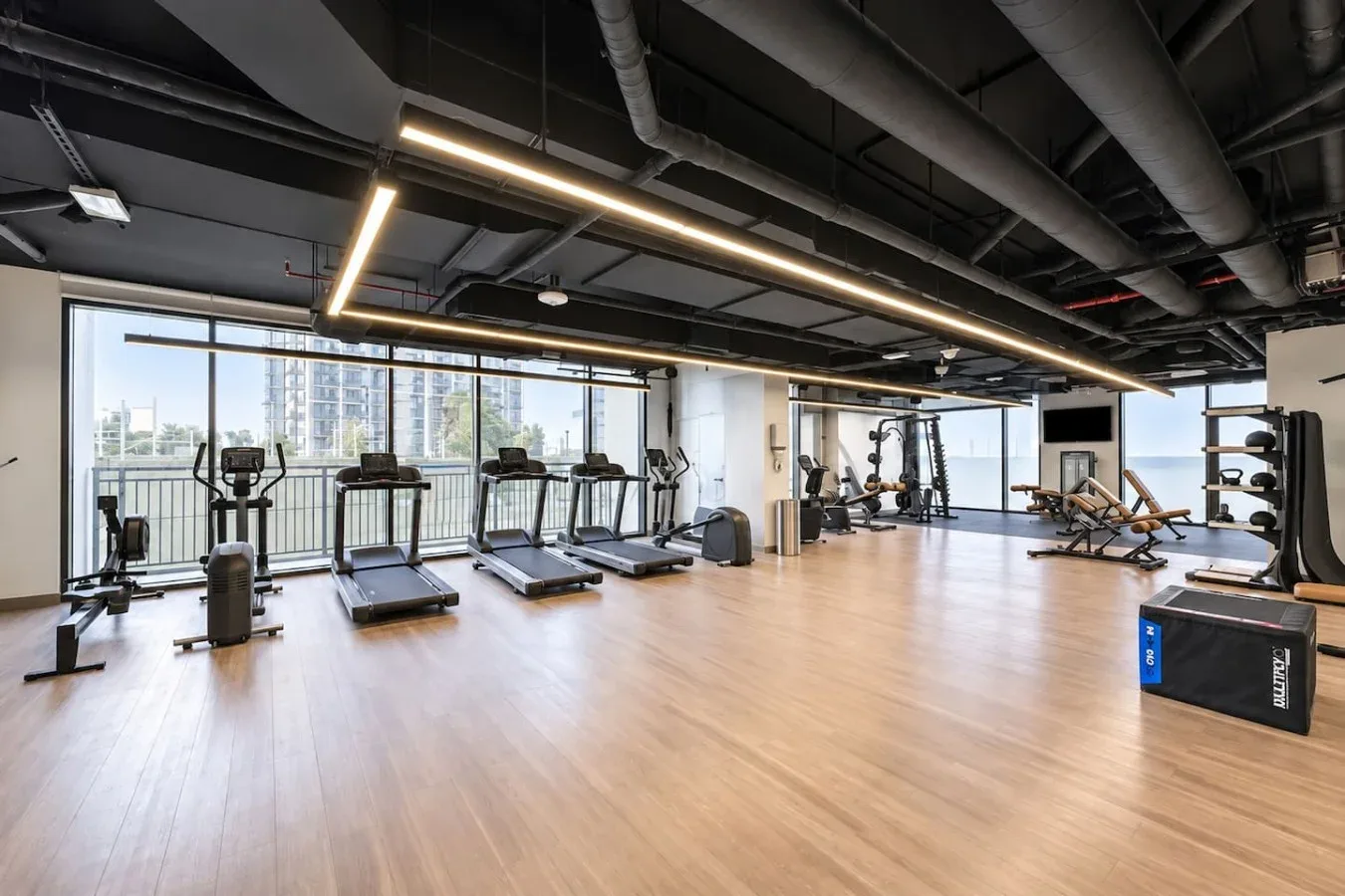 Un gimnasio amplio con equipos de ejercicio junto a ventanales de piso a techo.