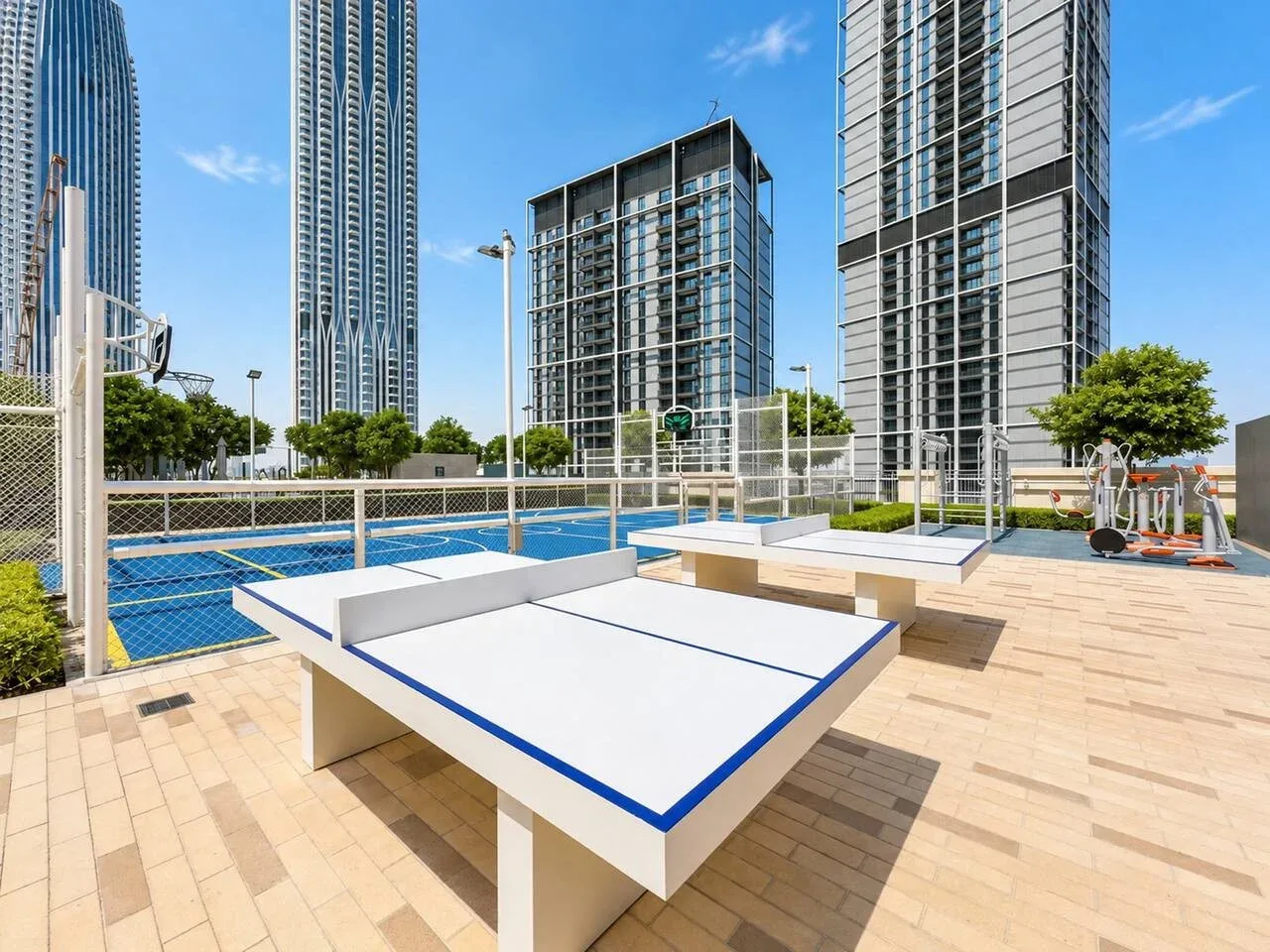 Zona recreativa al aire libre con una mesa de ping-pong de superficie azul y edificios altos al fondo.