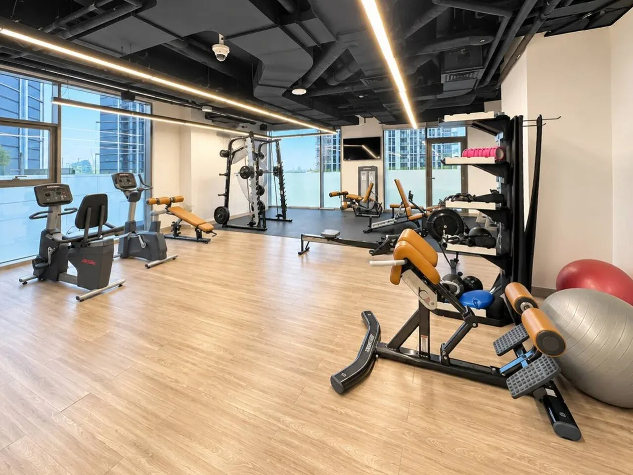 Un gimnasio con máquinas de ejercicio y equipo de entrenamiento junto a grandes ventanas.