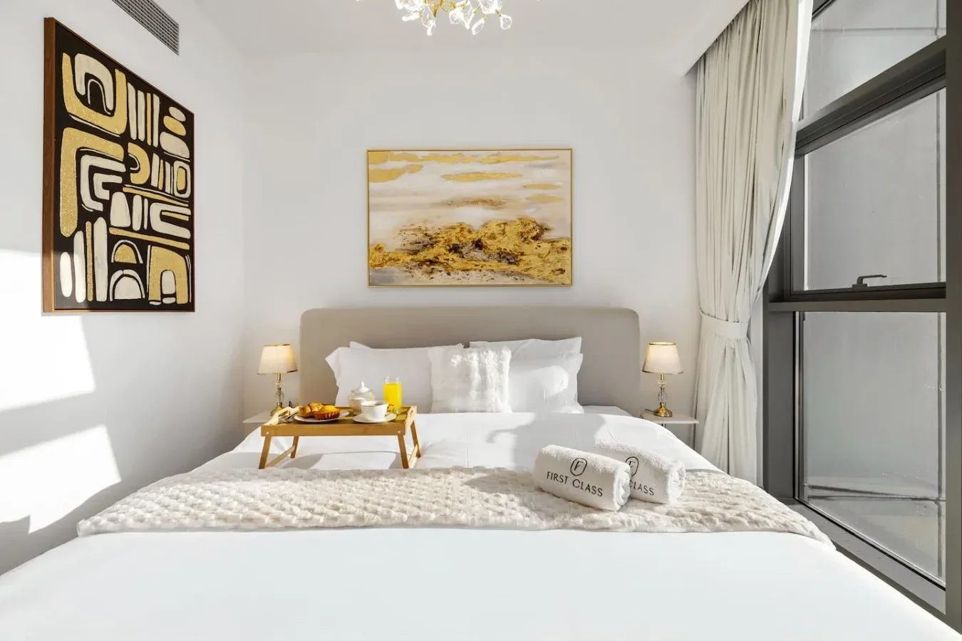 Un dormitorio luminoso con una cama hecha, lámparas de noche y grandes ventanas.