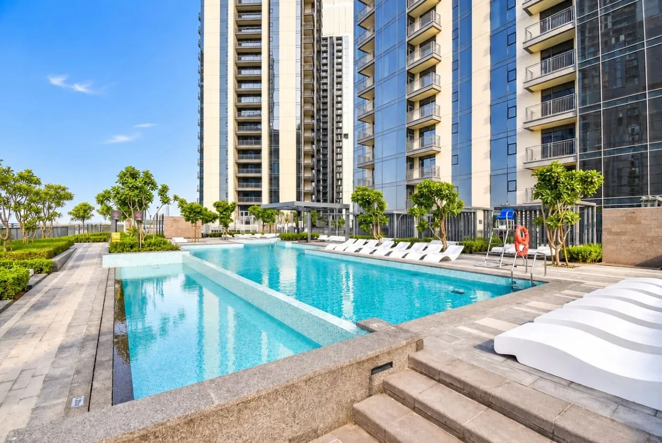 Una piscina con tumbonas está rodeada de edificios modernos de gran altura.