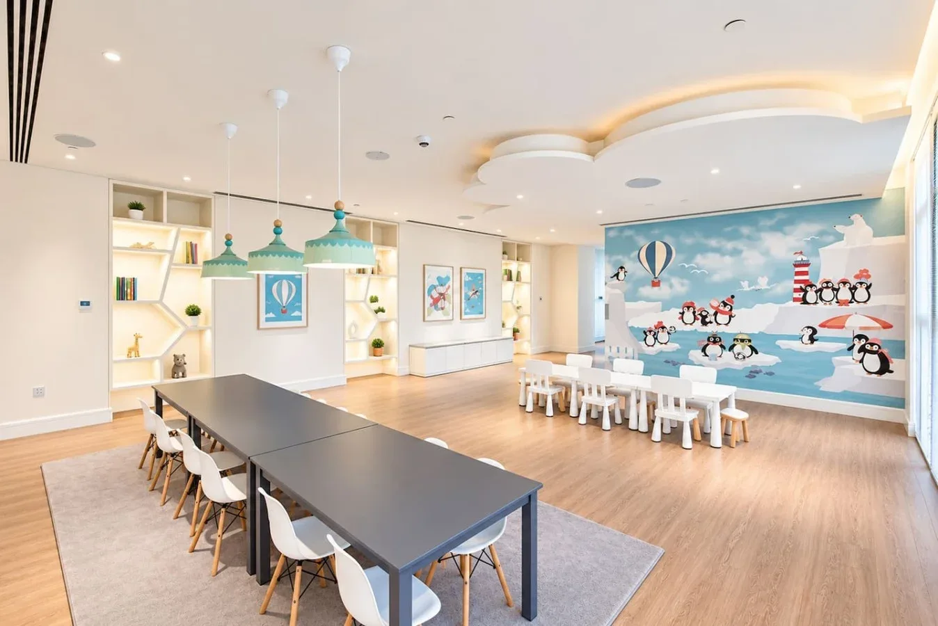 Un luminoso comedor y sala de juegos infantil tiene mesas largas y un mural colorido junto al mar.