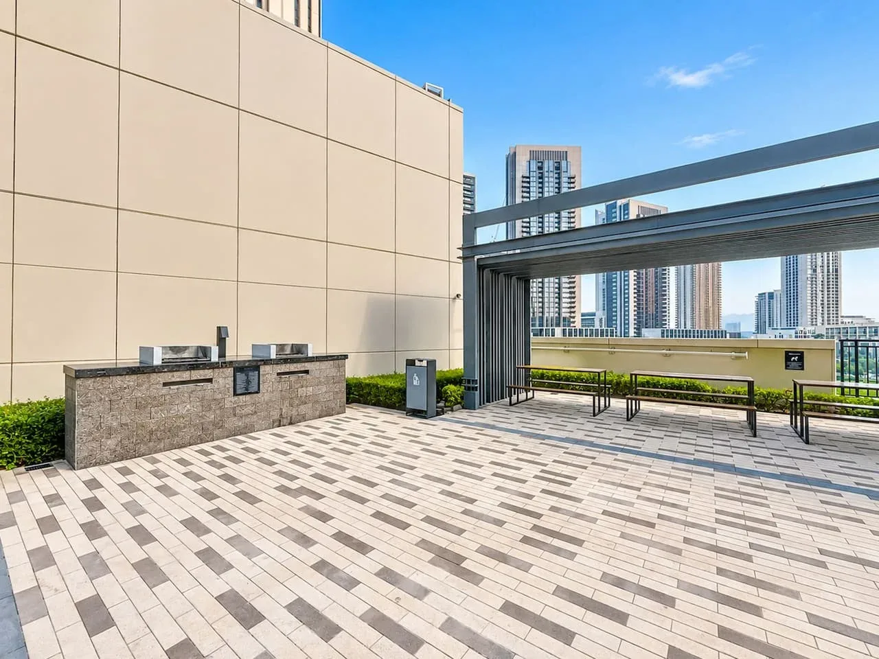 Una terraza en la azotea con suelo pavimentado, asientos integrados y edificios al fondo.