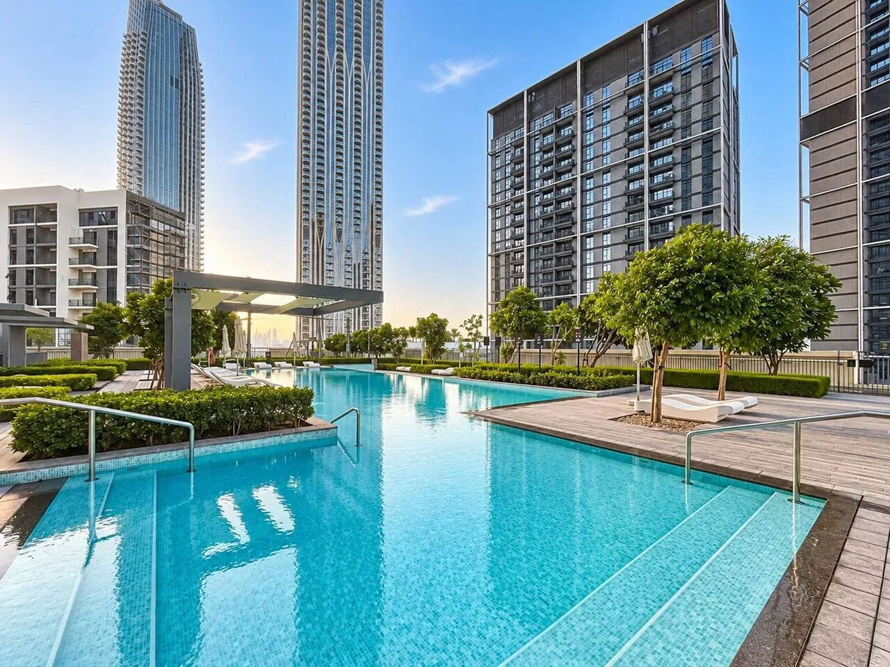 Una piscina al aire libre se encuentra entre edificios modernos de gran altura y jardines.
