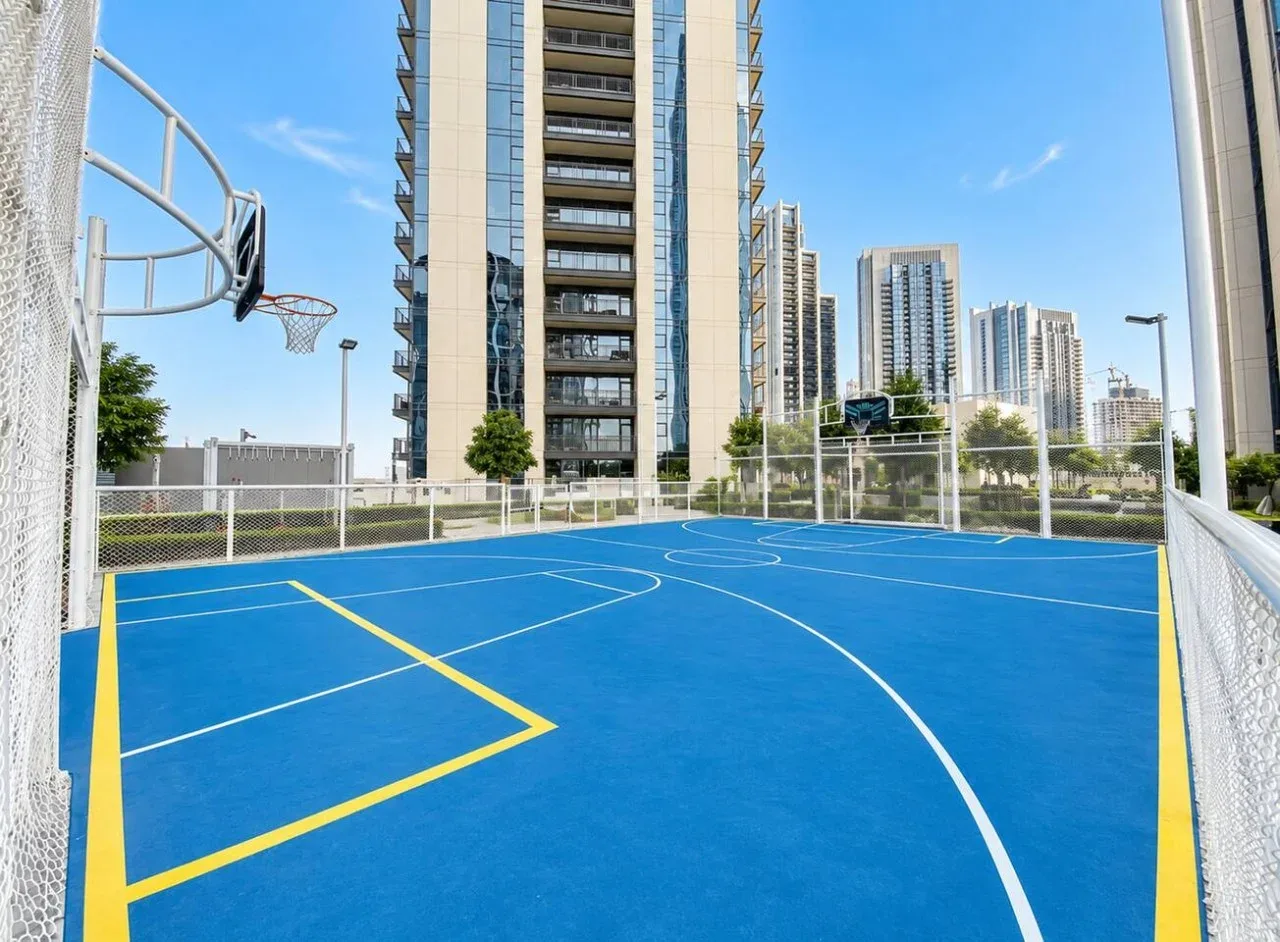 Una cancha de baloncesto al aire libre con suelo azul y edificios altos al fondo.