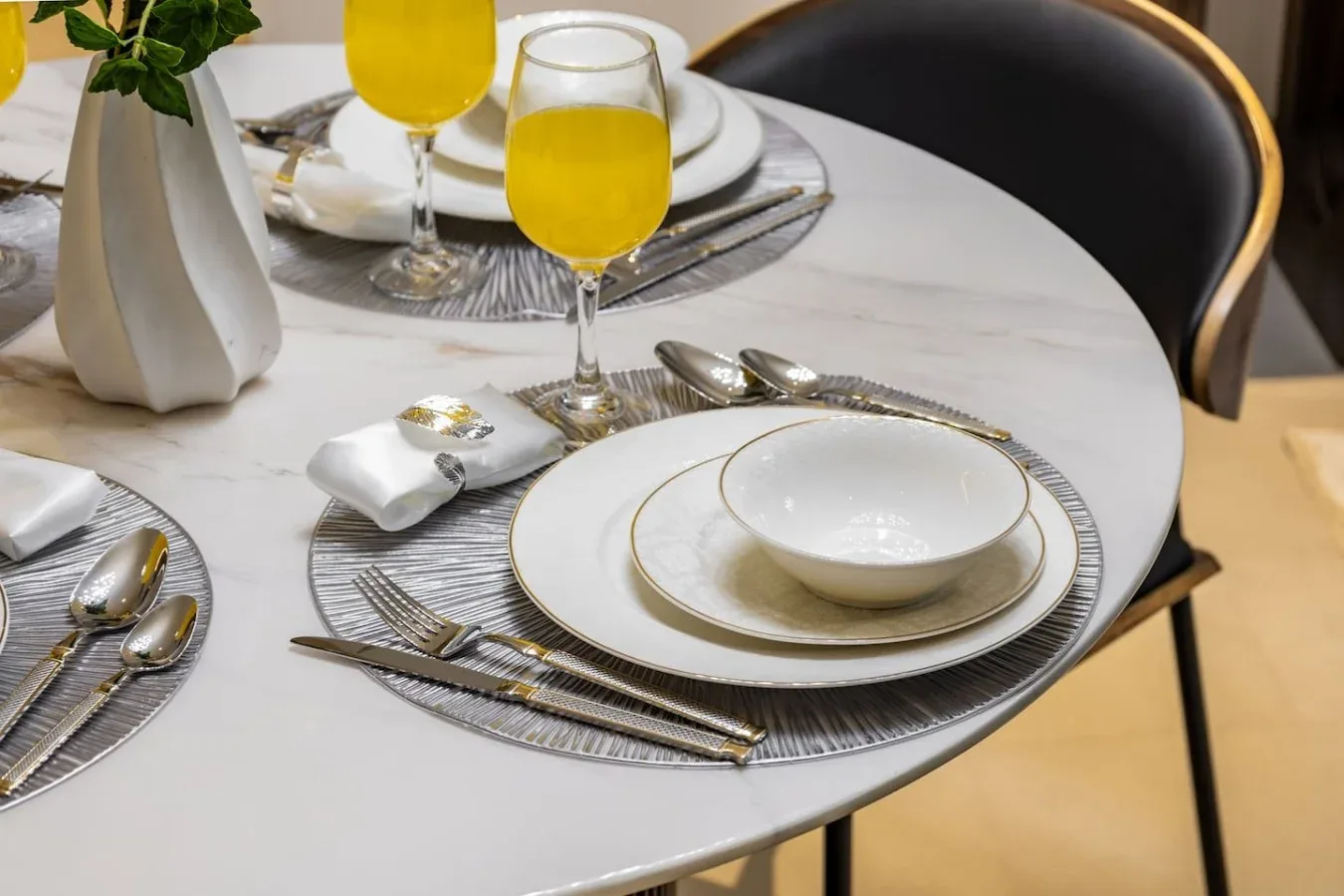 Una mesa de comedor está preparada con platos, cubiertos y vasos de zumo de naranja.