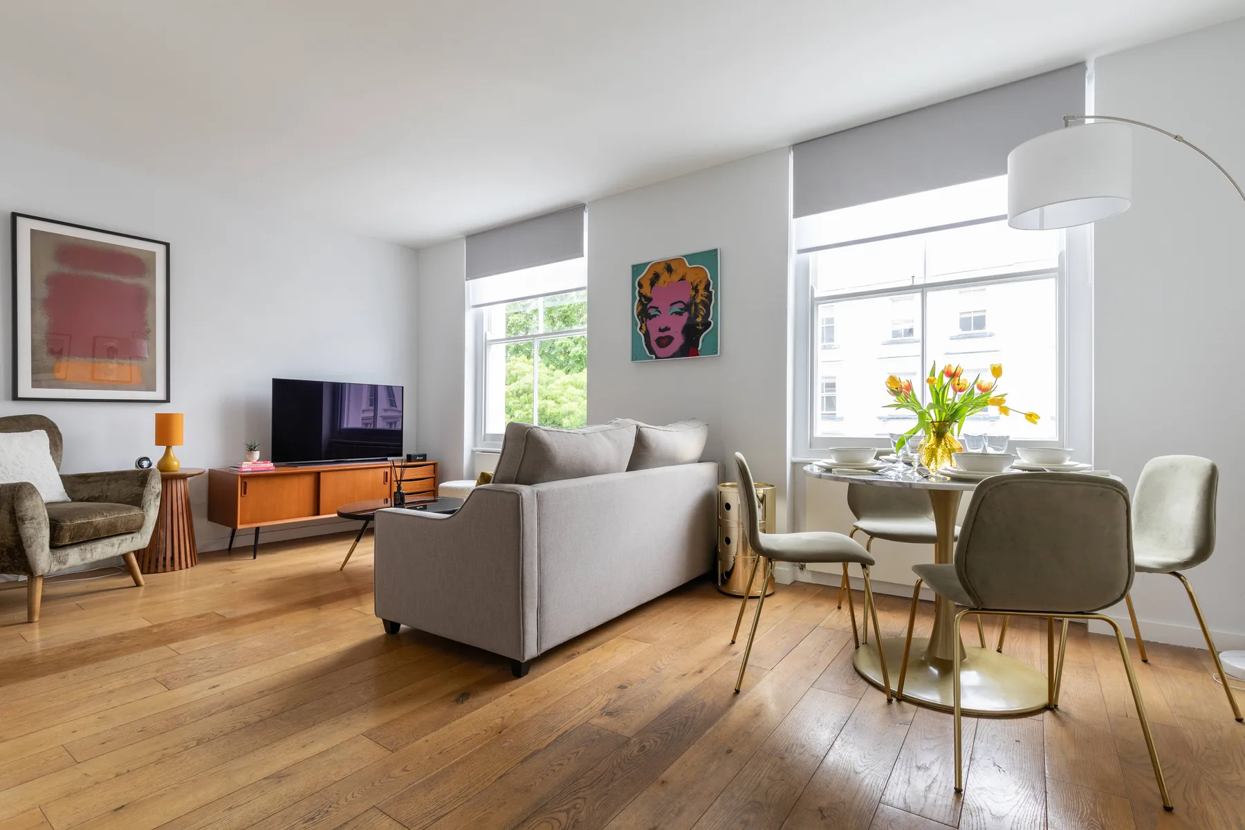 Una luminosa sala de estar y comedor con sofá, televisor y ventanales.