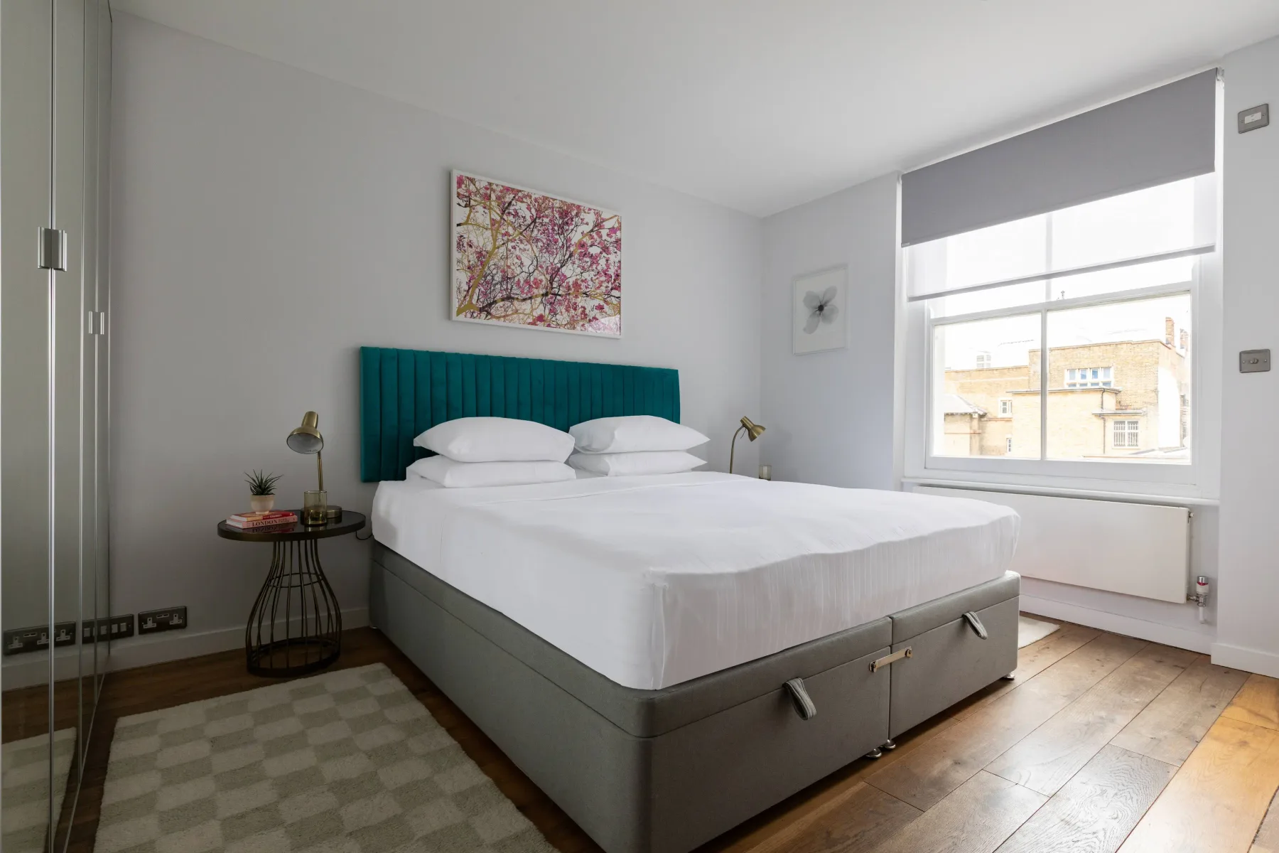 Dormitorio luminoso con una cama grande, cabecero verde azulado y ventana amplia.