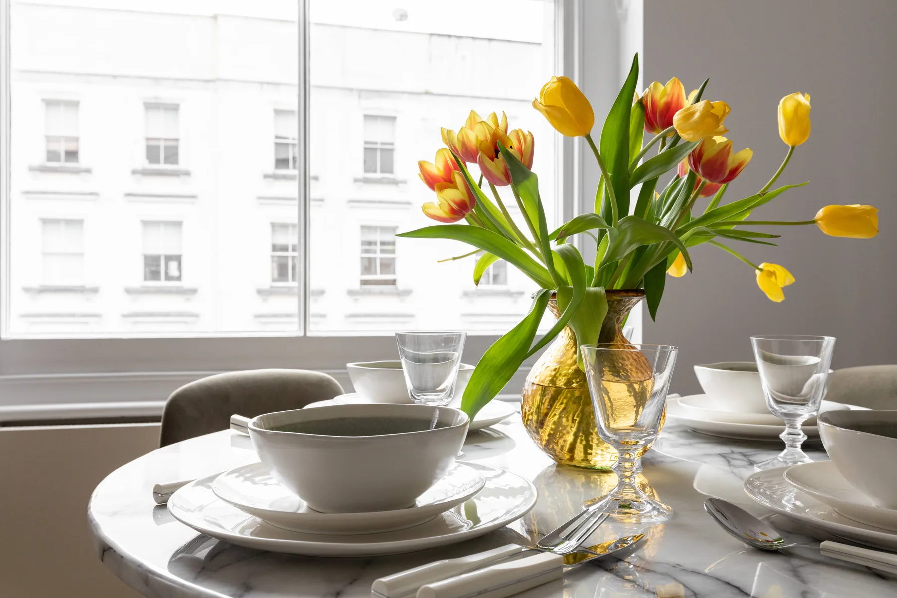 Una mesa de comedor está puesta con platos y copas junto a un jarrón de tulipanes.