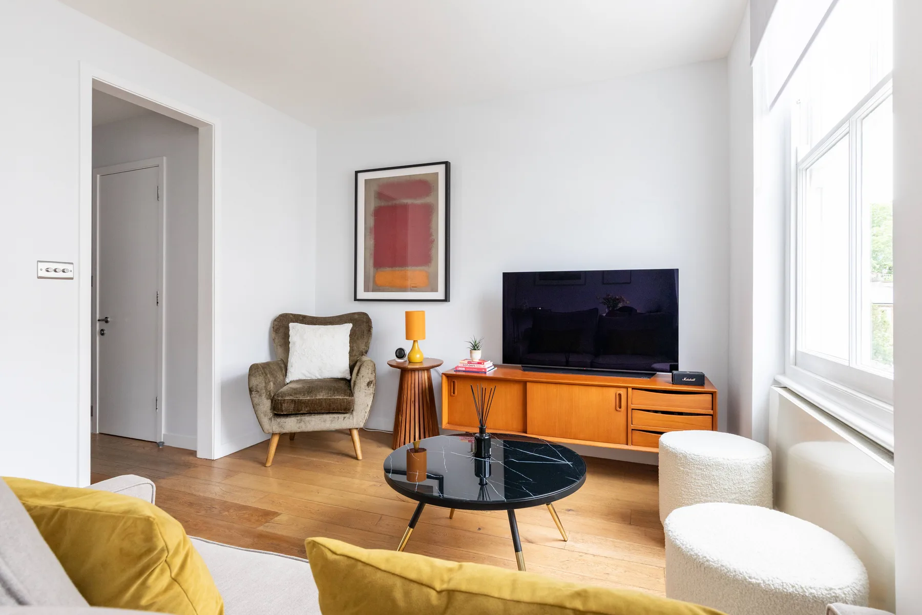 Una sala luminosa con televisor, mueble de madera y mesa de centro de vidrio.