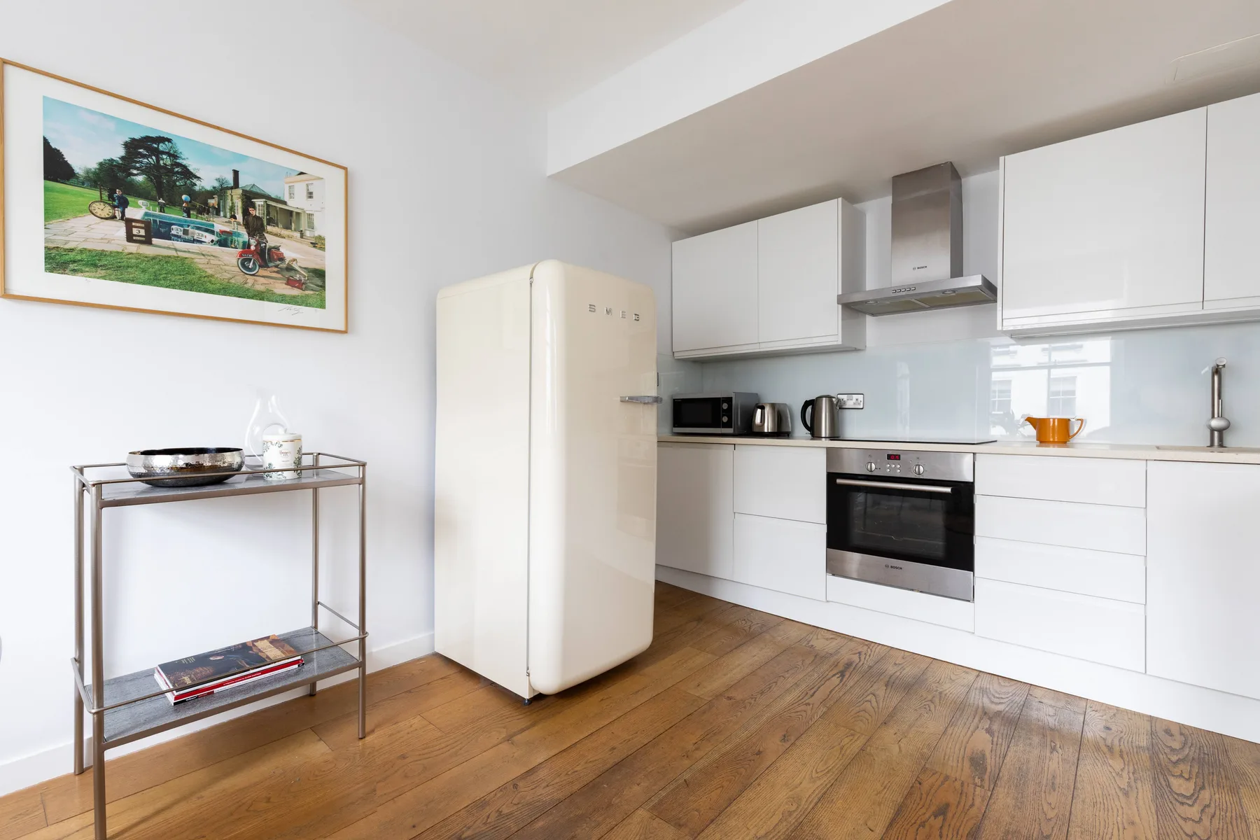 Una cocina luminosa con armarios blancos, un refrigerador y suelo de madera.