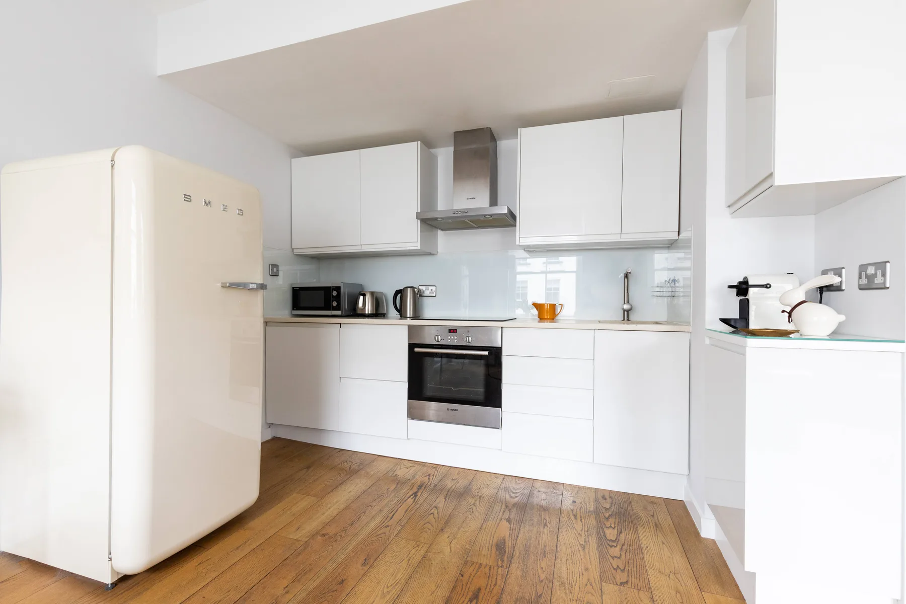Una cocina luminosa con gabinetes blancos, electrodomésticos y piso de madera.