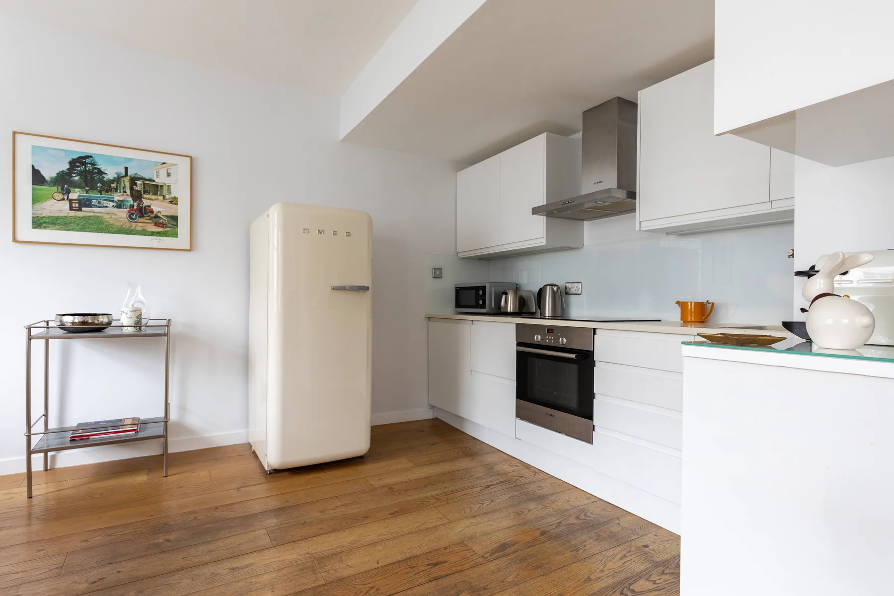 Una cocina luminosa con armarios blancos, un refrigerador y suelo de madera.