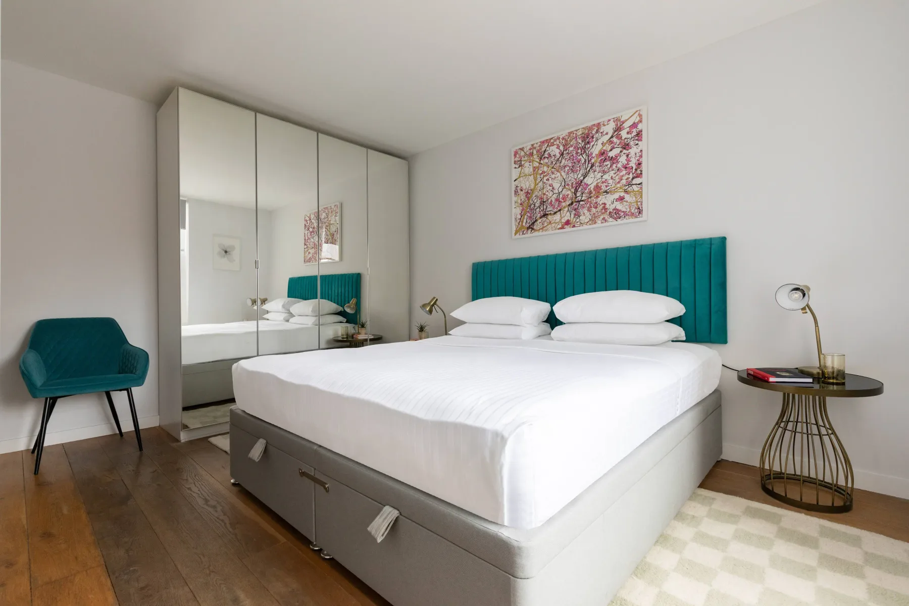 Un dormitorio con una cama blanca, un cabecero verde azulado y un armario con espejo.