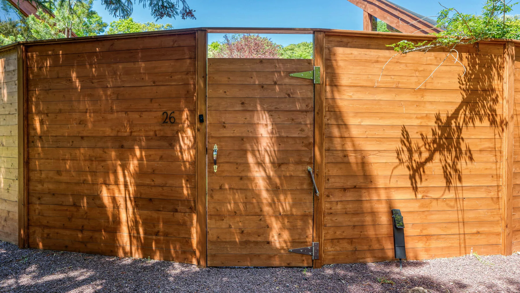 Una cerca de madera con una puerta cerrada está bajo árboles frondosos.