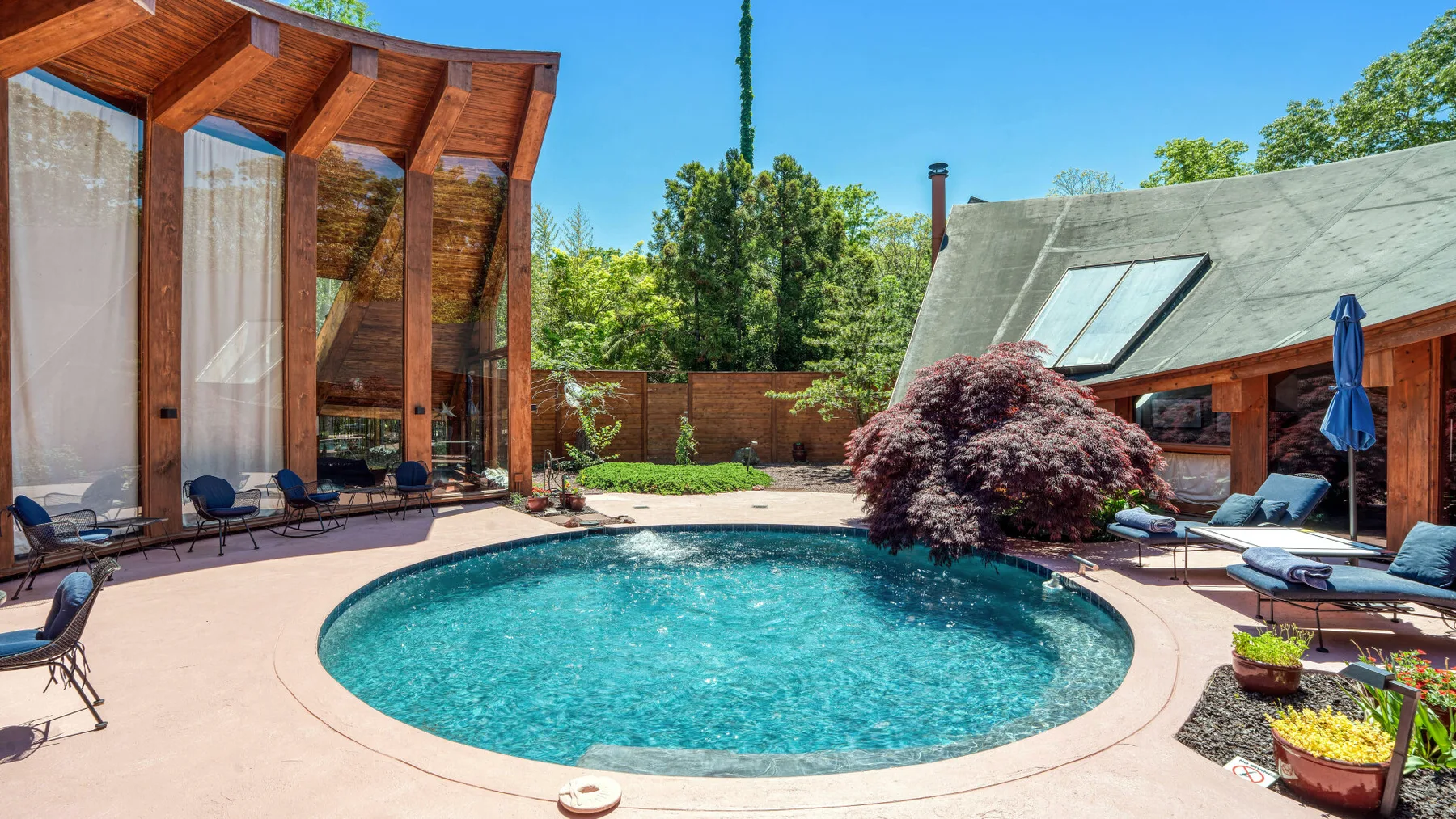 Una piscina al aire libre junto a un patio de madera y un jardín con plantas.