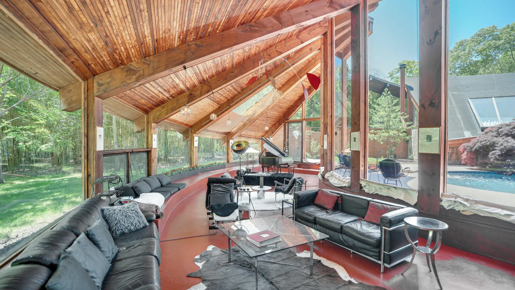 A bright living room with seating beneath a sloped wooden ceiling and tall windows.