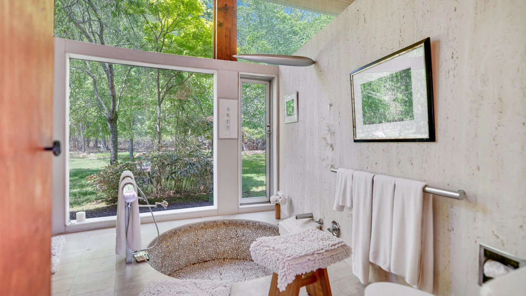 Un baño luminoso con una gran ventana que da a una zona verde.