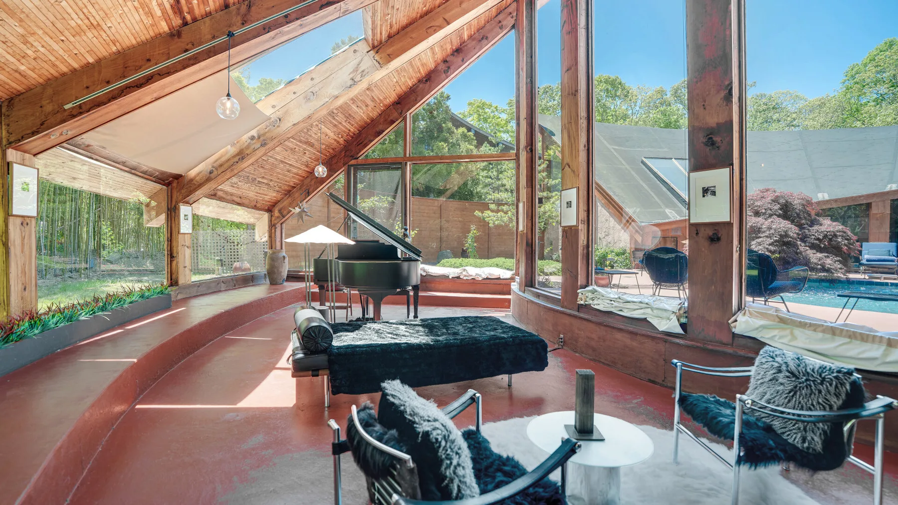 A sunlit music room with a grand piano and seating beneath a wood-beamed ceiling.