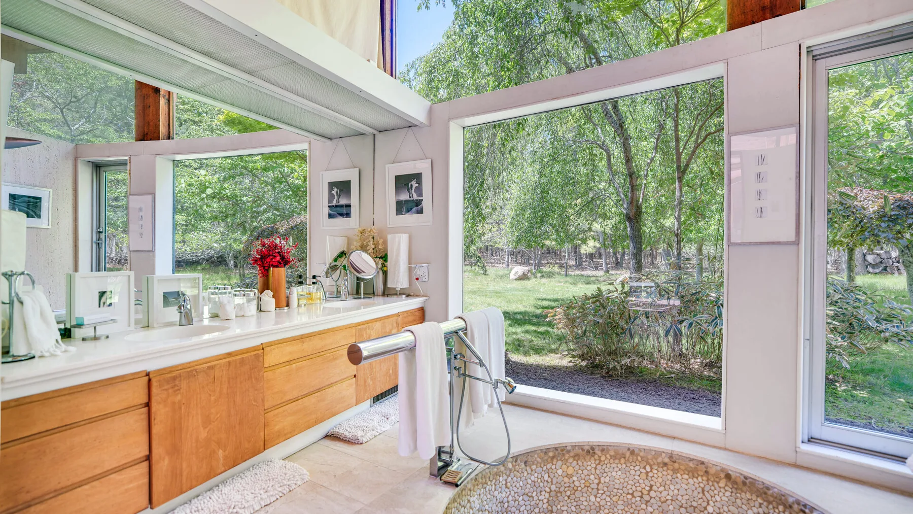 Un lavabo de baño con un espejo grande da a un jardín frondoso.