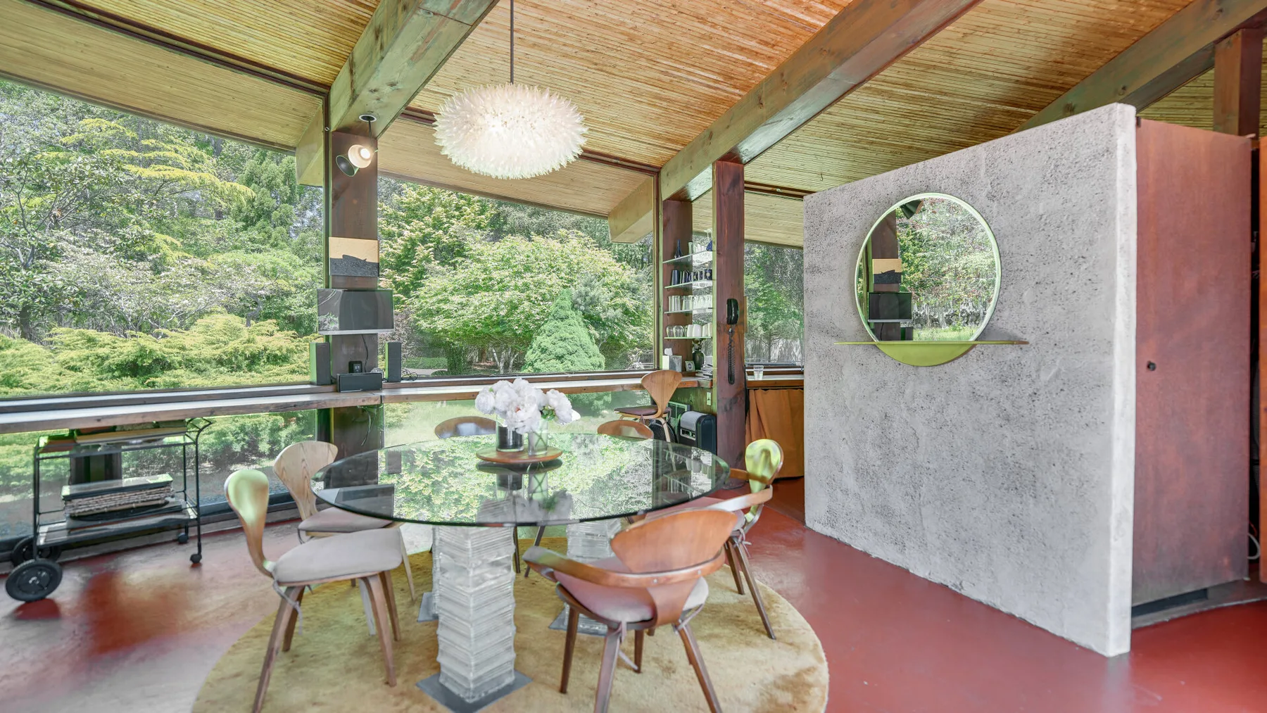 Un comedor cubierto con una mesa de vidrio y vistas a una vegetación frondosa.