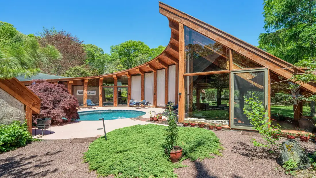 A modern house with a sloping timber roof overlooks a swimming pool and landscaped garden.