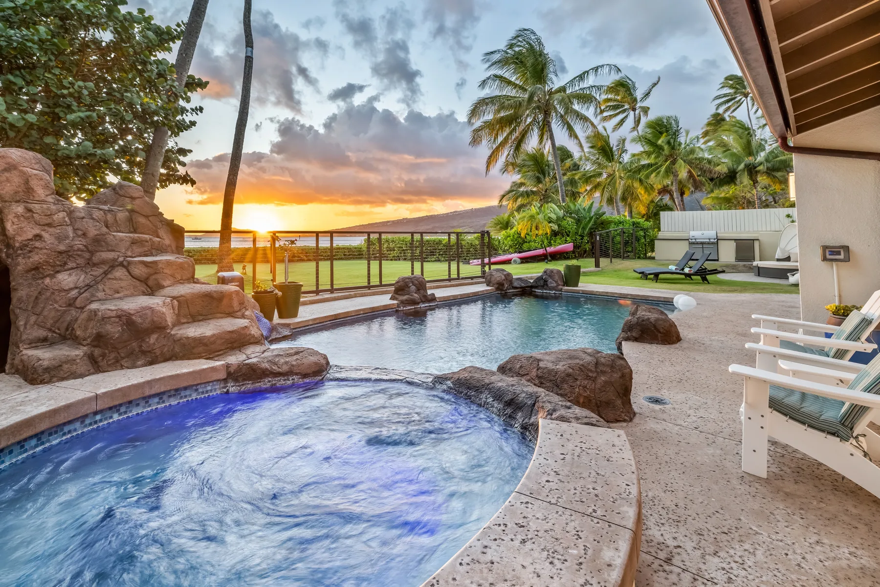 Una piscina exterior y un spa burbujeante dan a un jardín tropical al atardecer.