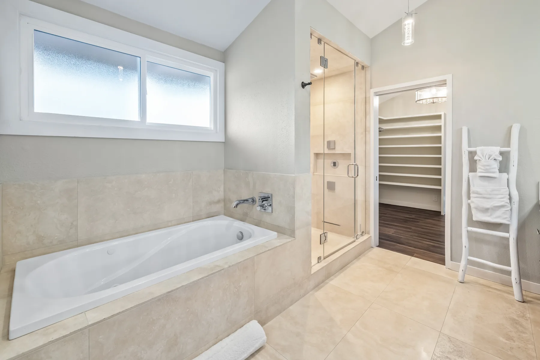 Un baño luminoso con bañera, ducha de vidrio y estantes abiertos.