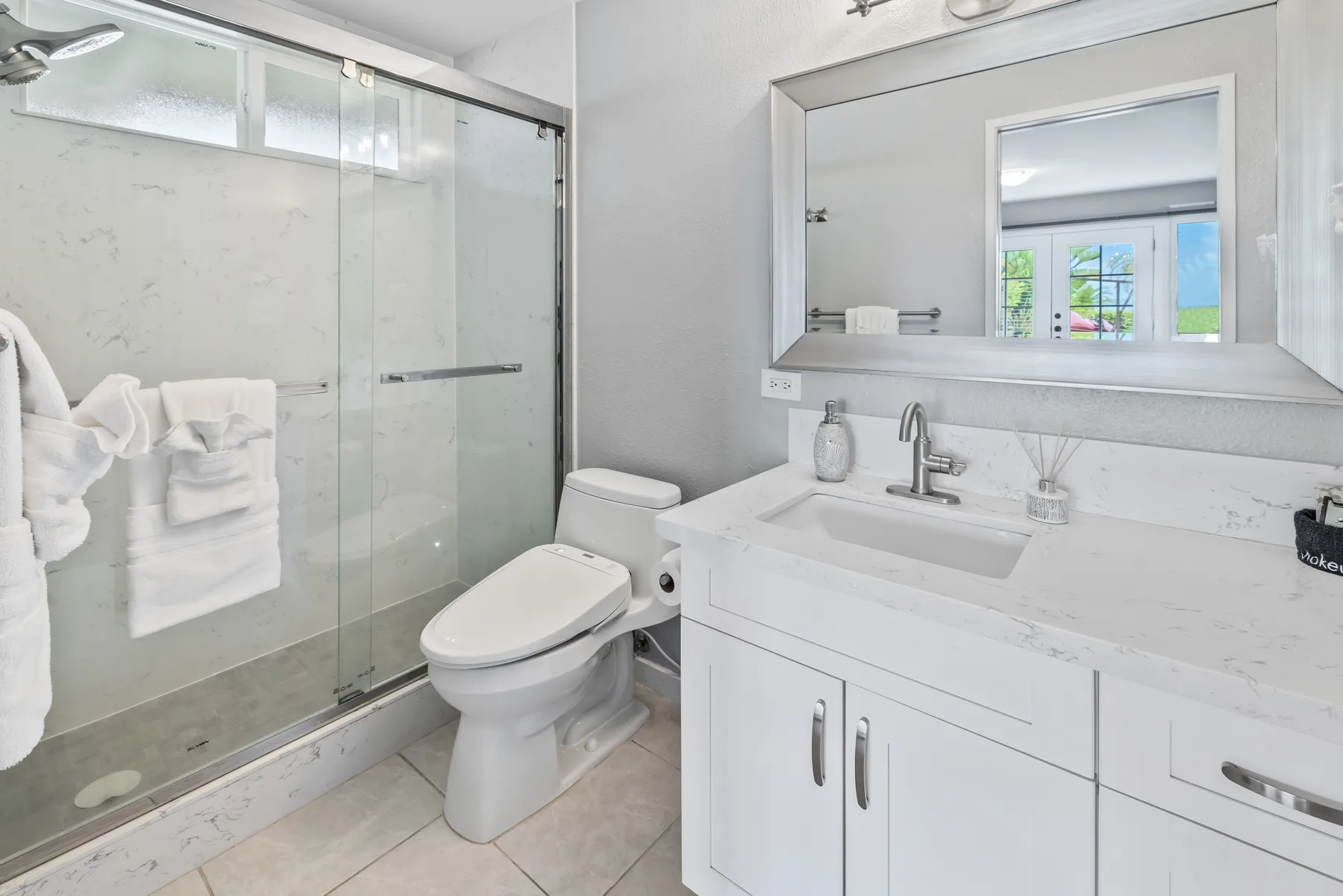 Un baño luminoso con ducha de vidrio, inodoro y tocador blanco.