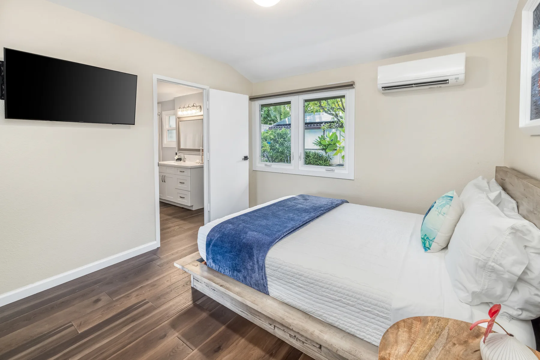 Un dormitorio con una cama, un televisor en la pared y una ventana con vegetación.
