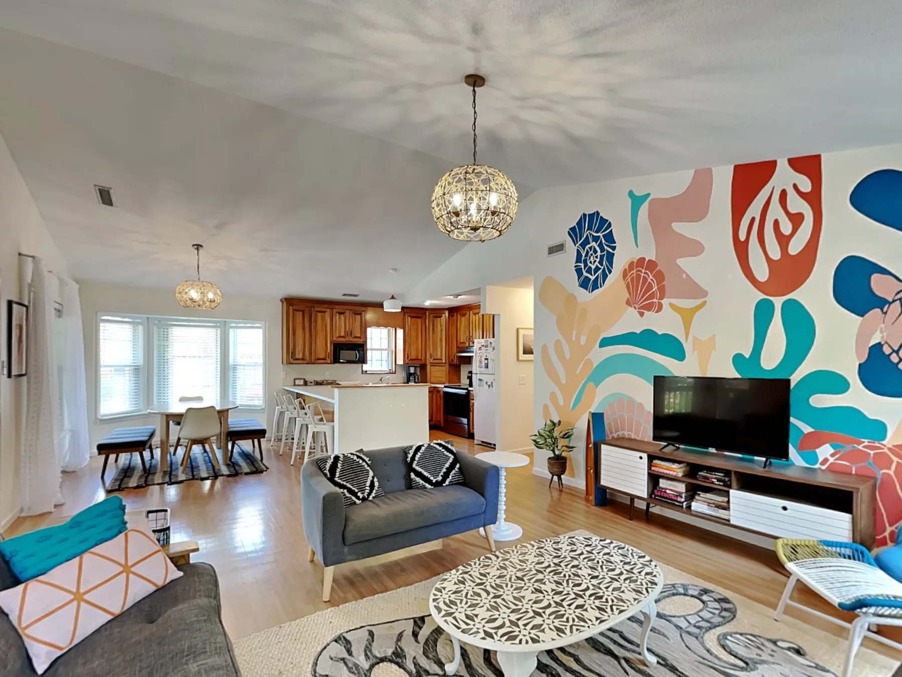 An open-plan living room with a colorful mural behind the television.