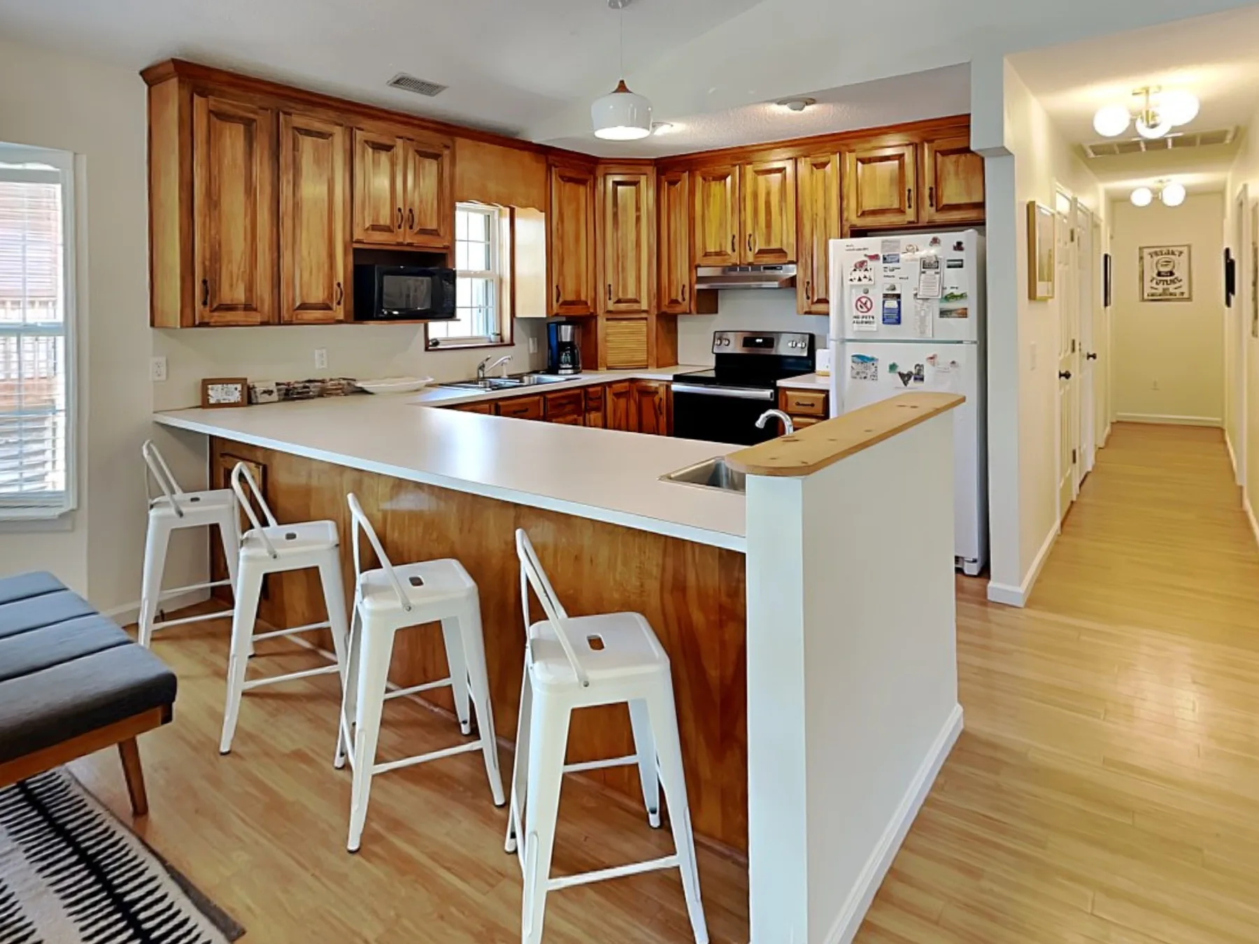 A kitchen with wooden cabinets, a light countertop, and white seating.