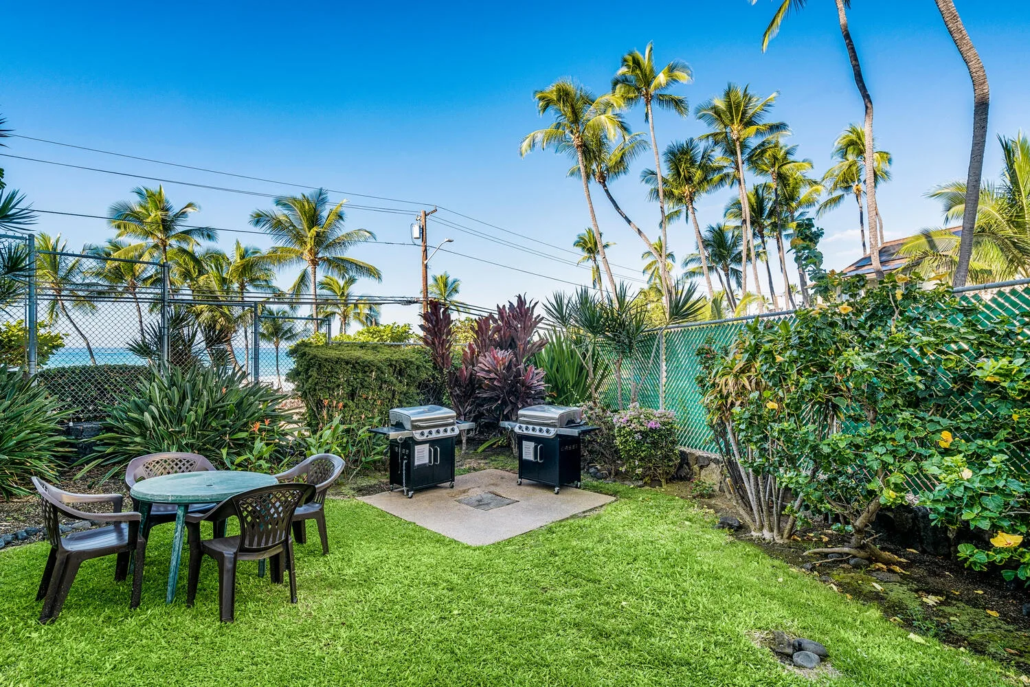 Un patio ajardinado con asientos al aire libre y parrillas, rodeado de plantas tropicales.