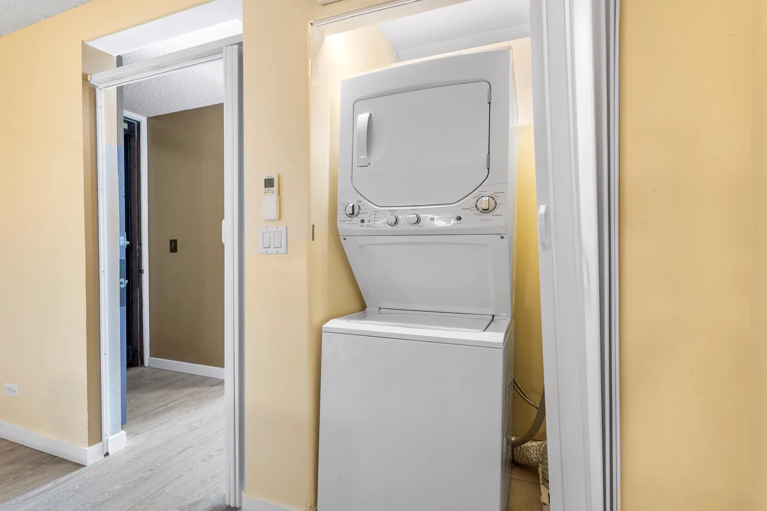 Una lavadora y secadora apiladas están en un armario junto a una puerta abierta.
