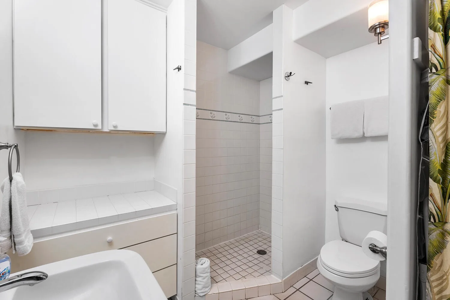 Un baño luminoso con ducha de azulejos, lavabo e inodoro.