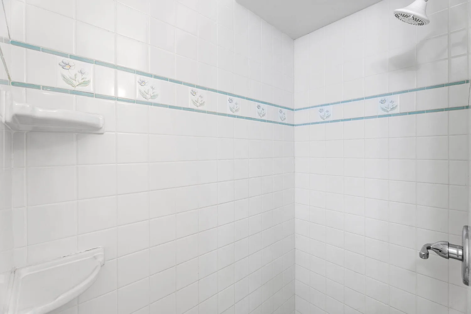 Una zona de ducha alicatada con una franja decorativa y un cabezal de ducha.