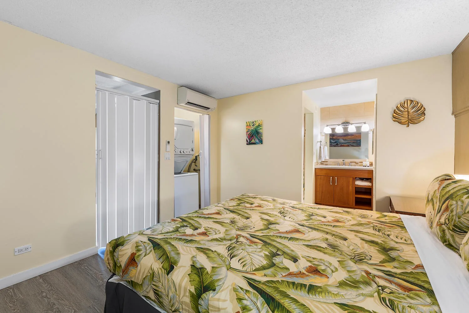 Un dormitorio con una colcha estampada de hojas y un tocador visible a través de la puerta.