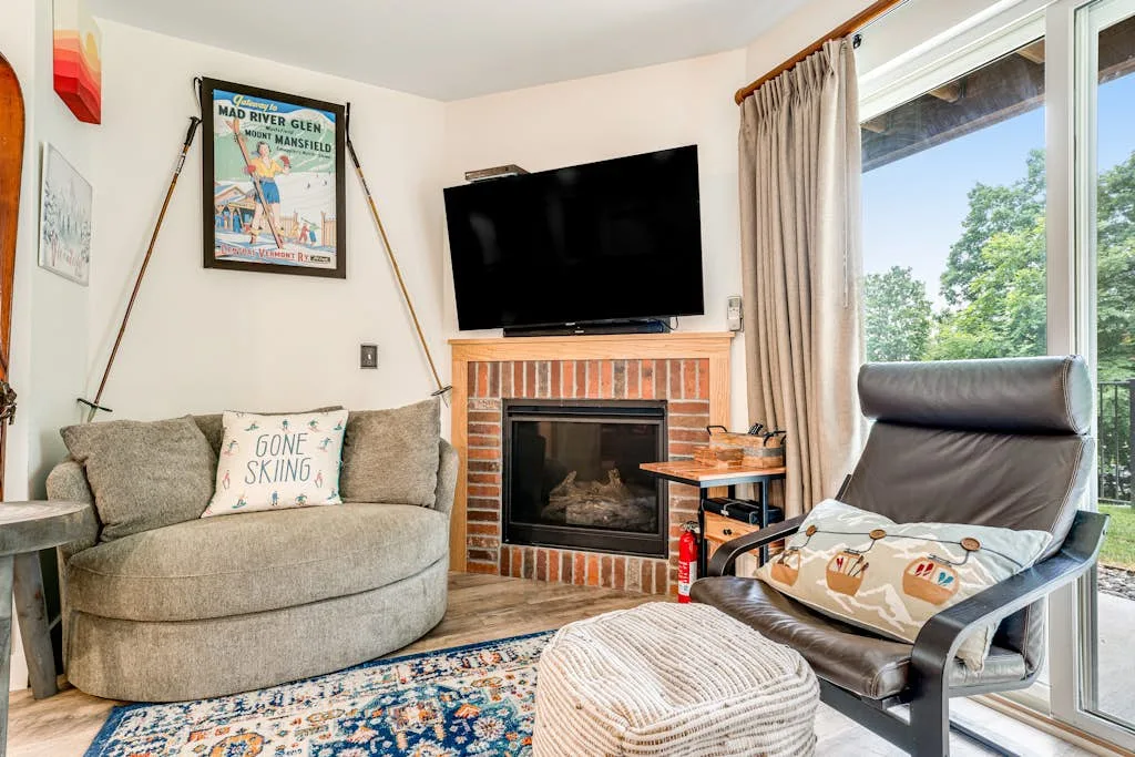 A living room with seating, a brick fireplace, and a television.