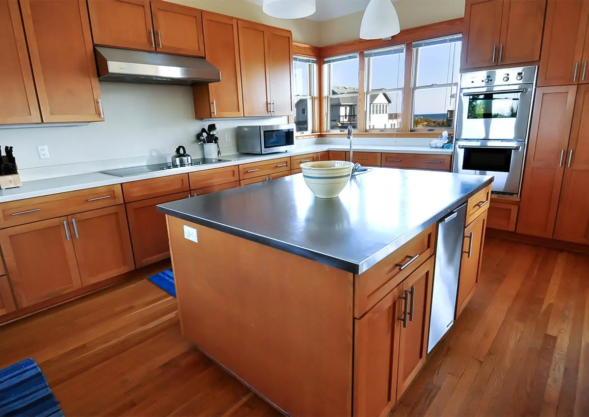 Una cocina luminosa con gabinetes de madera, una isla central y grandes ventanas.