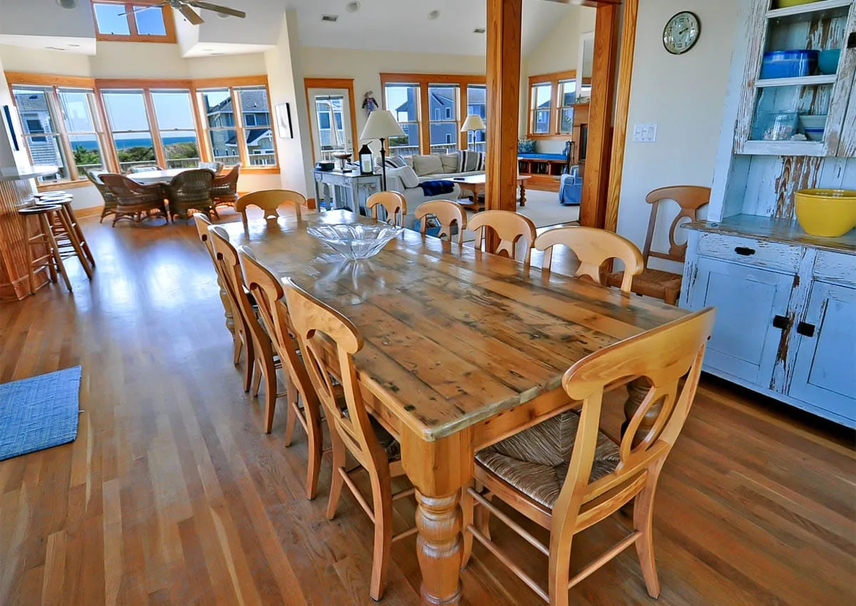 Comedor con una larga mesa de madera y sillas junto a una sala luminosa.