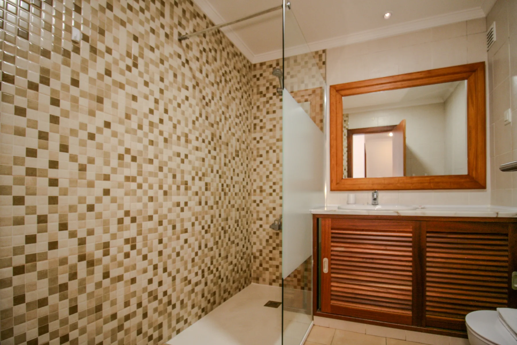 A tiled bathroom with a glass shower and a wooden vanity.