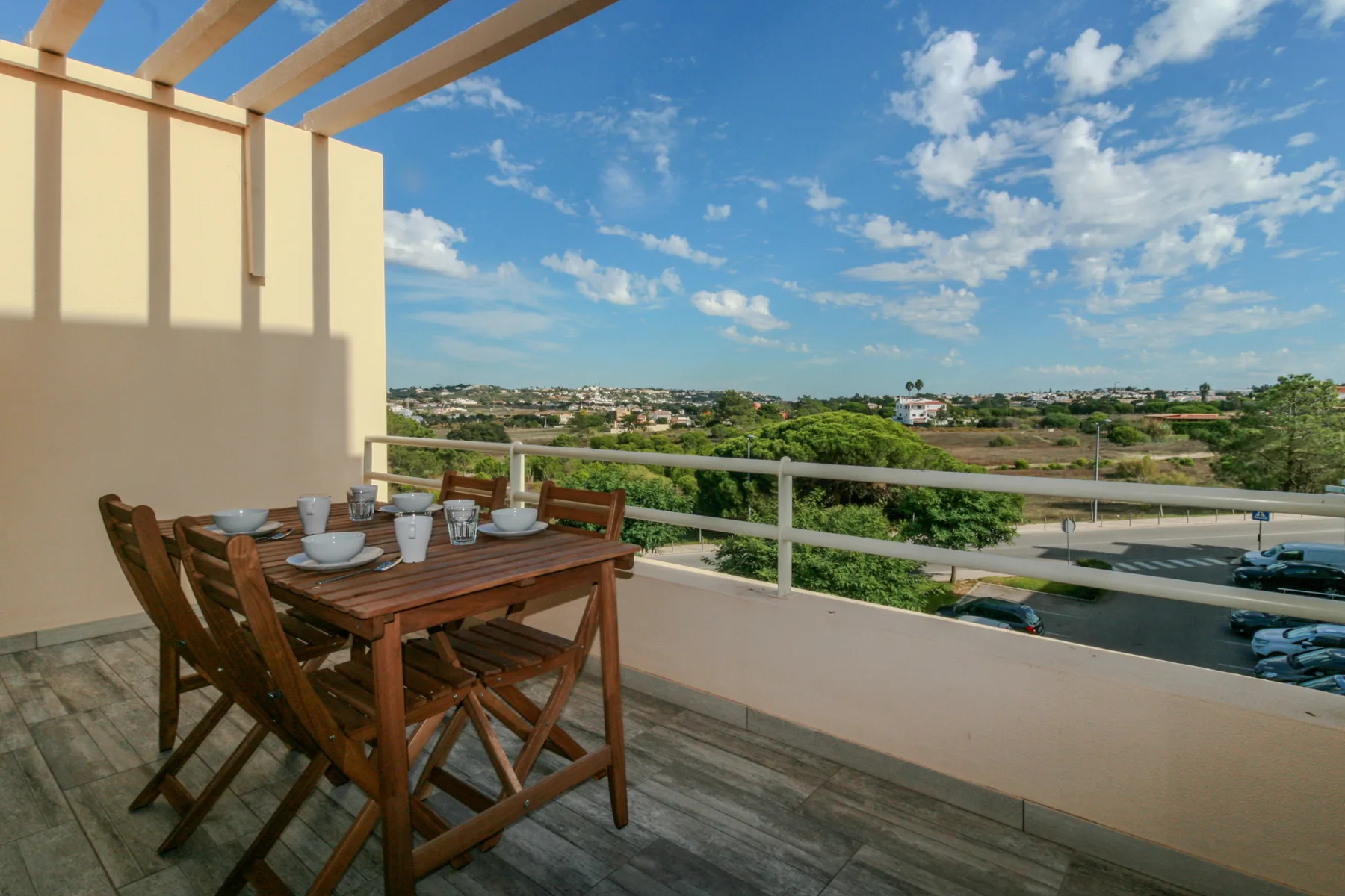 A furnished balcony overlooks greenery and a distant neighborhood.