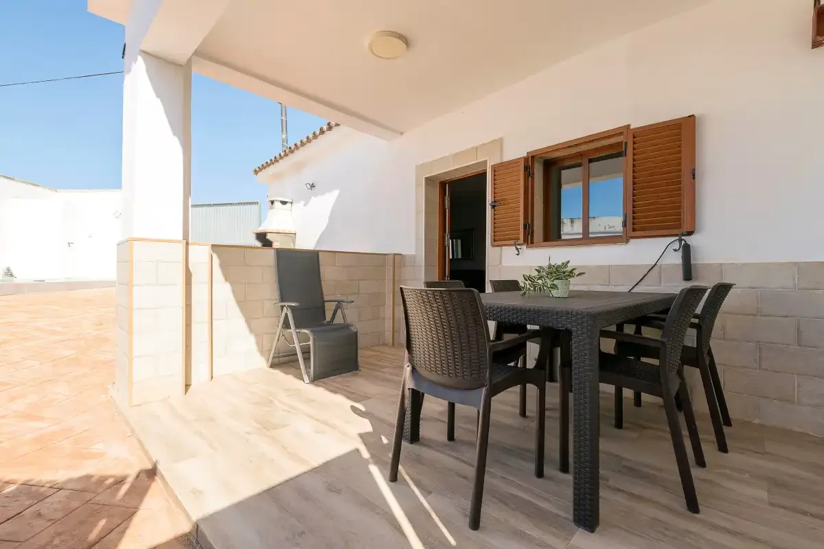 A covered outdoor dining area with a table and seating beside an open doorway.