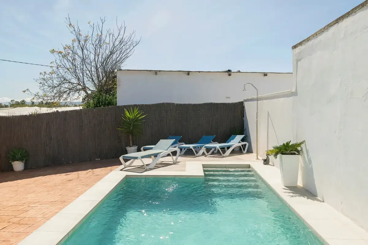 An outdoor pool with lounge seating beside white walls.