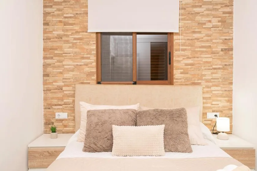 A bedroom with a bed beneath a window set in a textured wall.